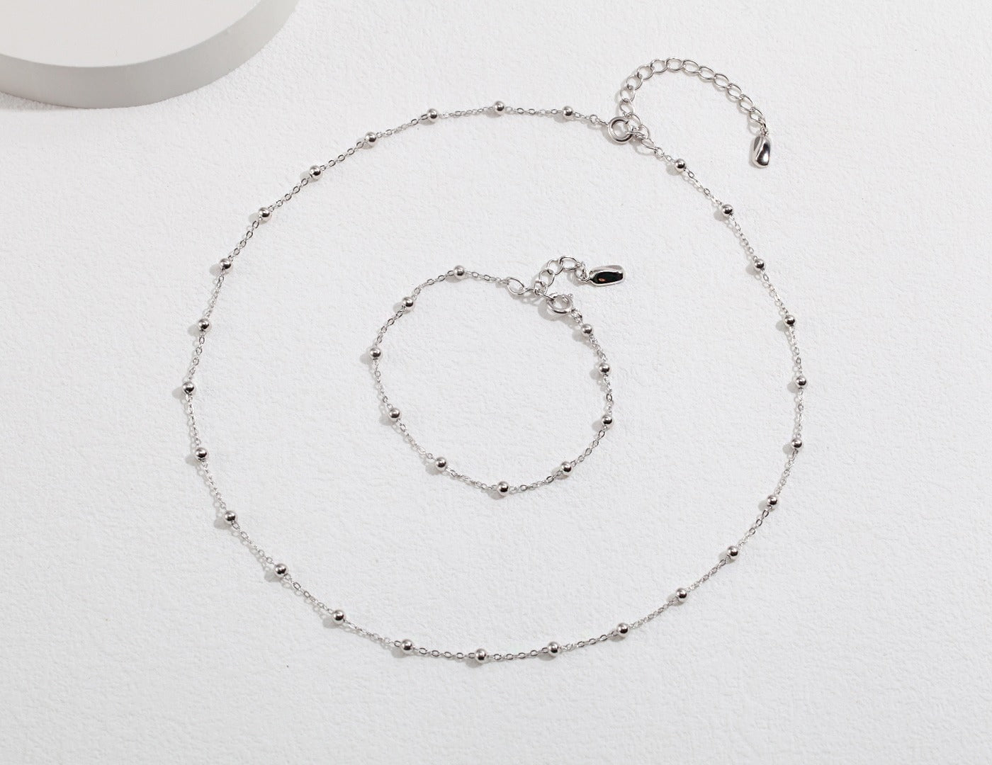  Enhance your style with a silver necklace and bracelet set featuring beautiful beads, displayed on a pristine white surface.