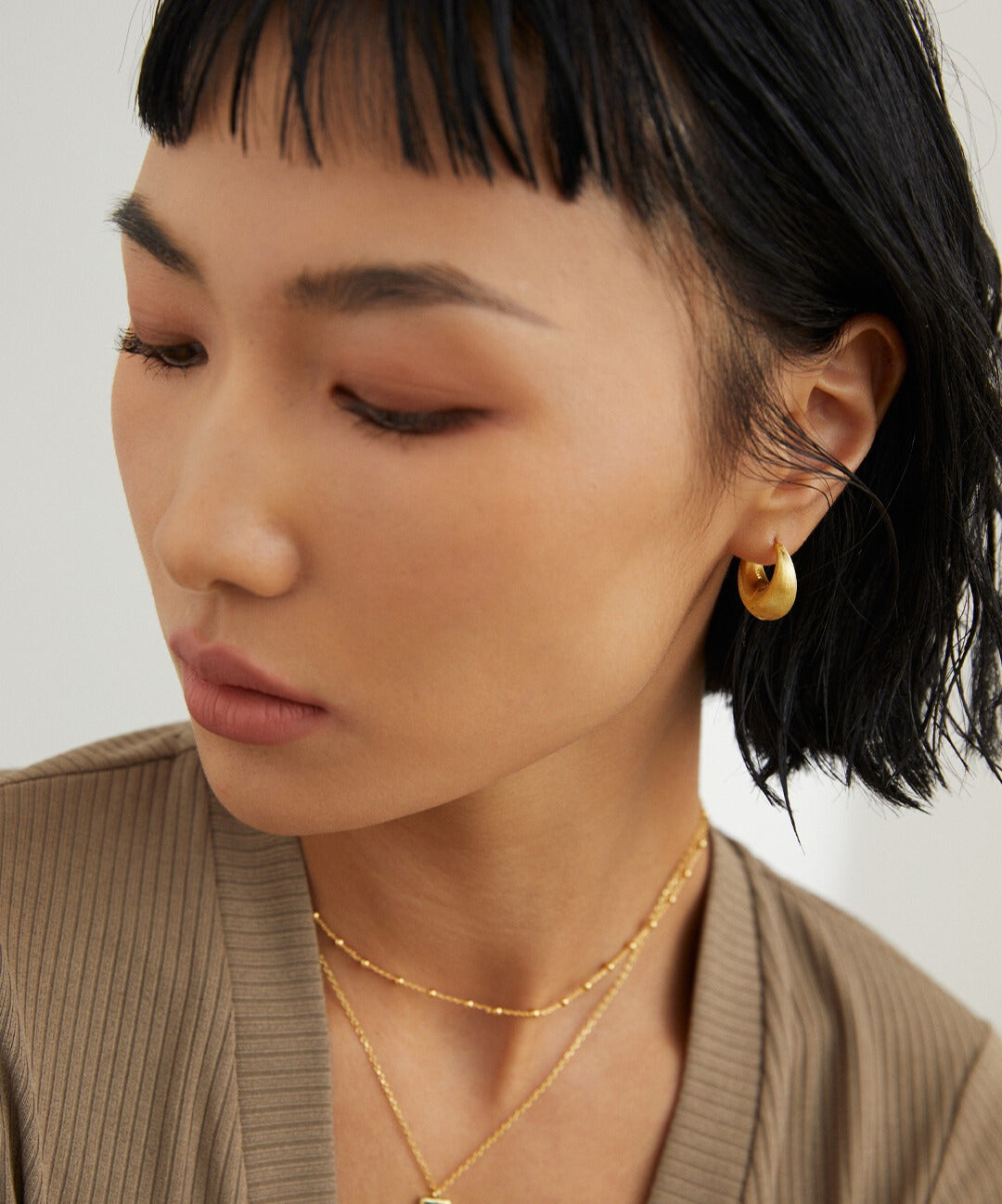 A woman wearing a gold necklace and earrings, with beads interspersed in the necklace.
