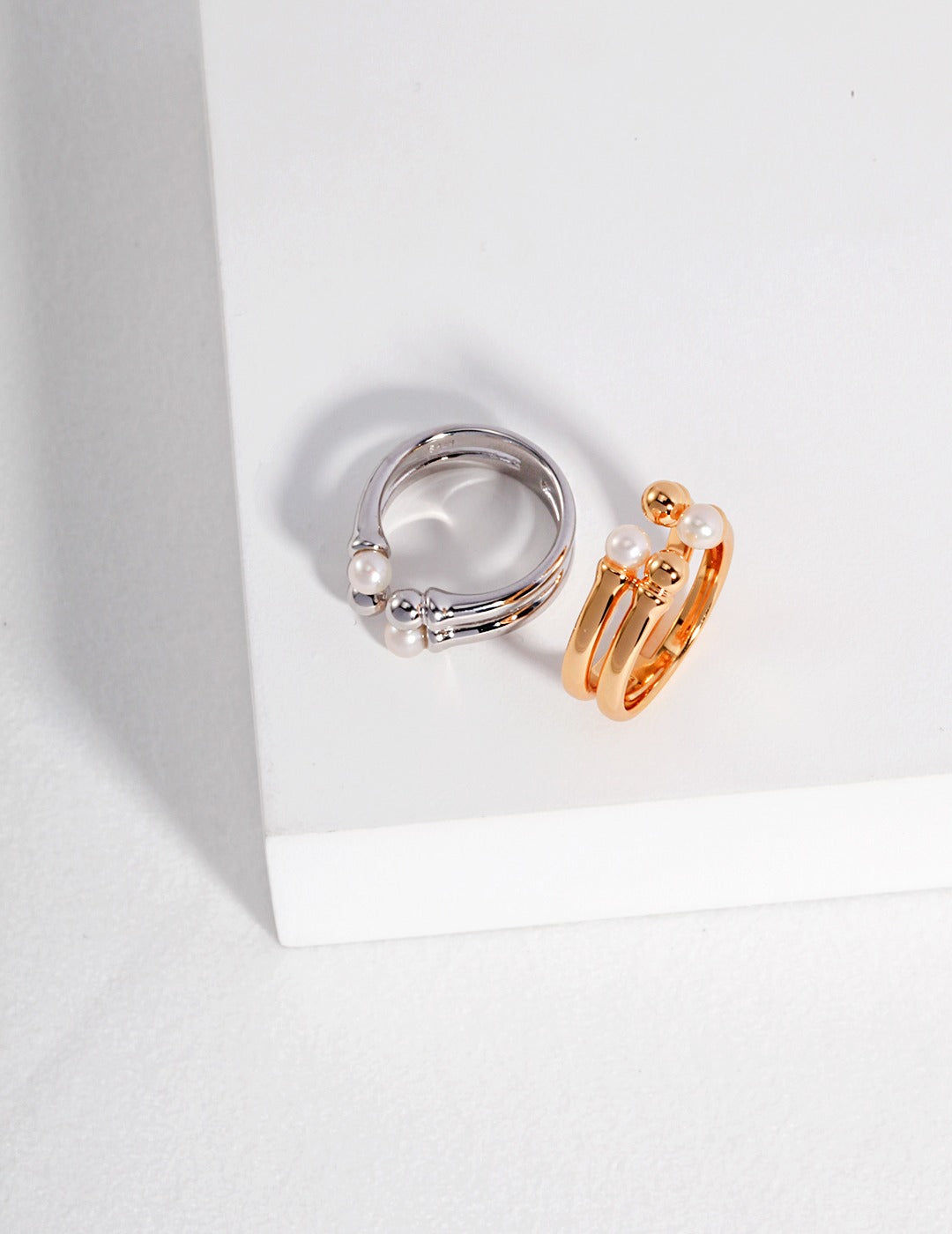 Silver and gold rings on a white surface, both adorned with dainty beads and freshwater pearls.