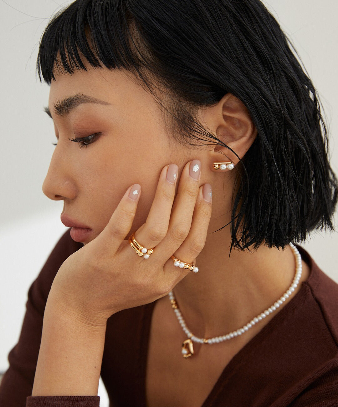 A model wearing gold jewelry, including a necklace and earrings, with a gold ring adorned with dainty beads and freshwater pearls.