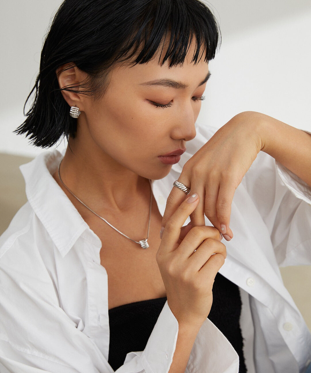 A model wearing a white shirt and a silver ring with a unique gear wheel texture.