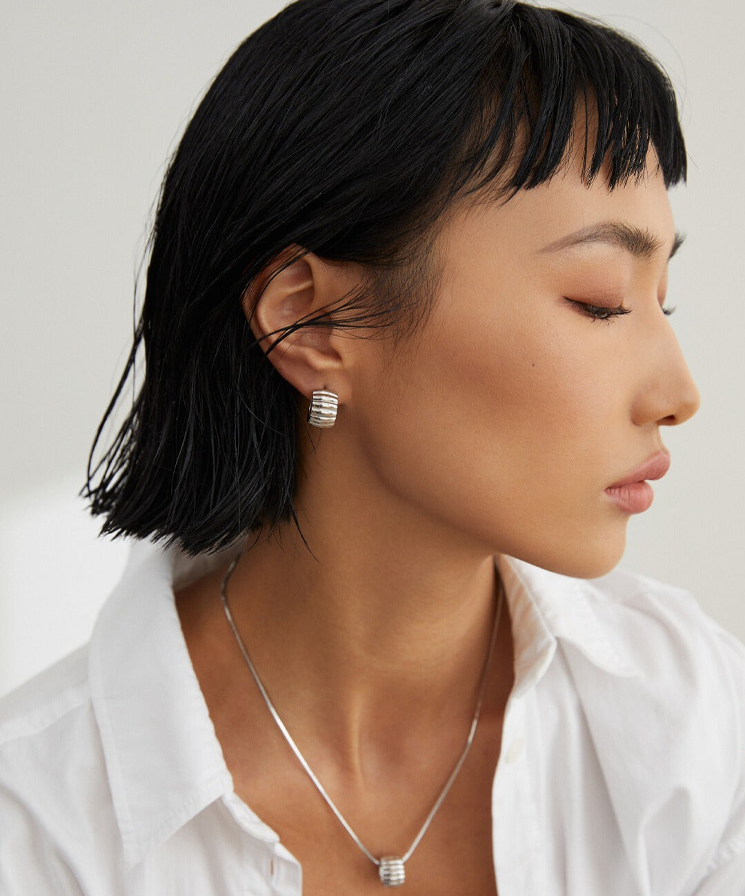 Stylish woman wearing white shirt and silver gear wheel textured jewelry.