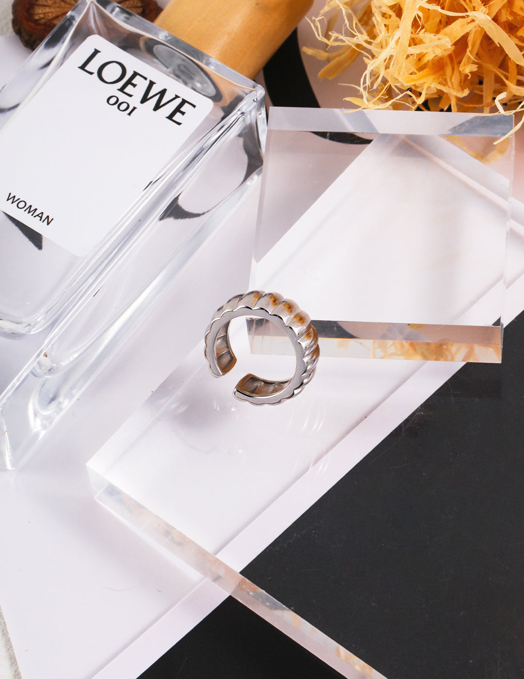 A bottle of perfume and a silver gear wheel inspired ring placed on a table, creating an elegant and stylish composition.