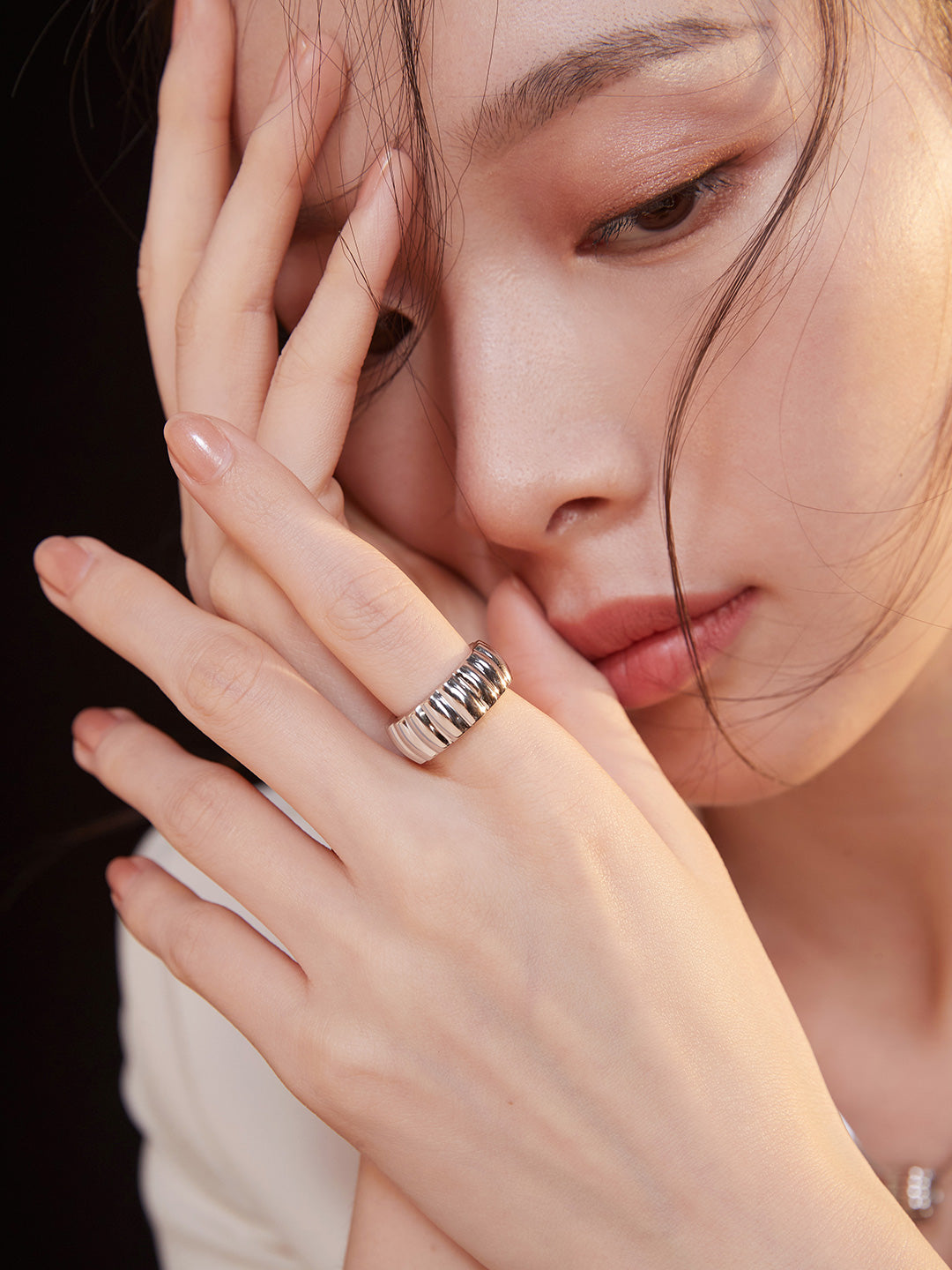 Model wearing silver gear wheel ring, hands on face.