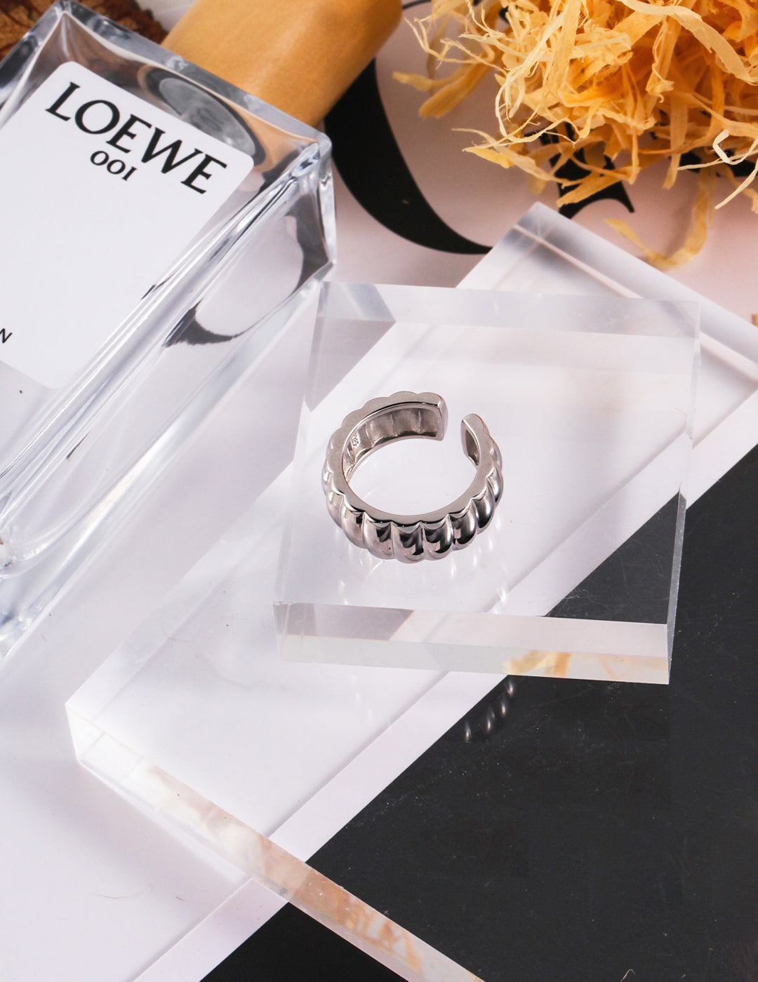 Table setting with silver gear wheel ring and bottle of perfume.