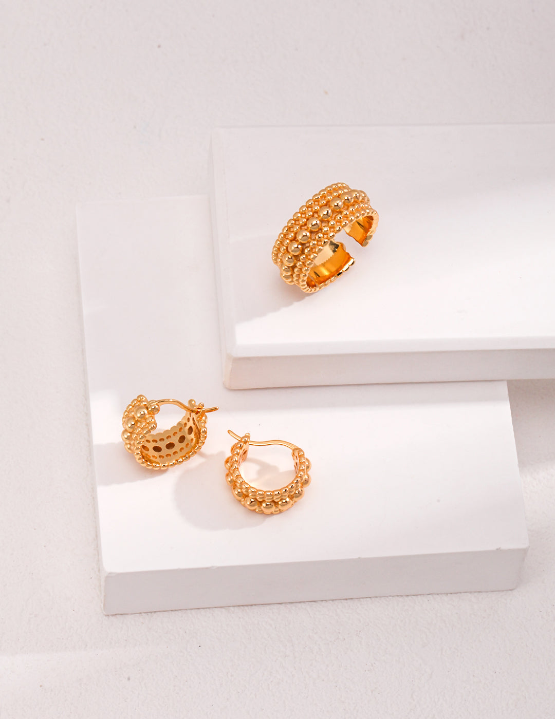 Gold plated hoop earrings with stacked bead layers, and a coordinating ring on white surface.