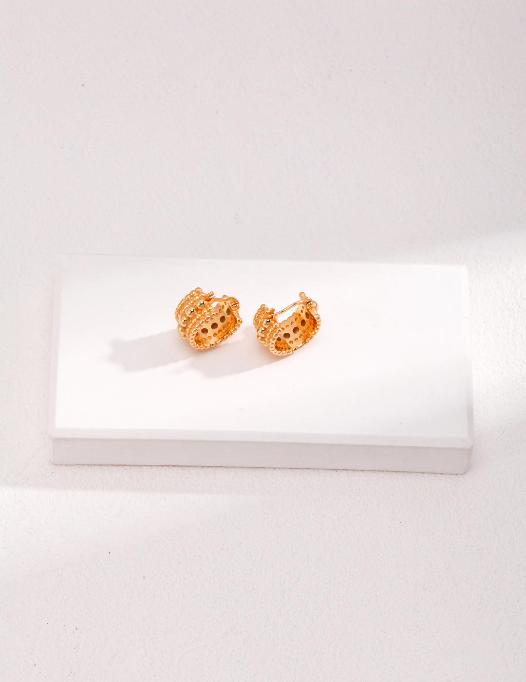 Two gold plated hoop earrings with stacked layers of beads, sitting on a white surface.