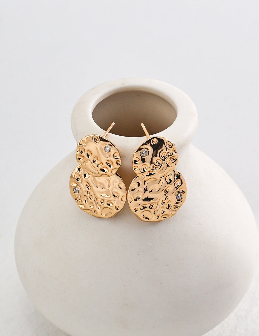 Stylish gold sculptured earrings placed on white vase.