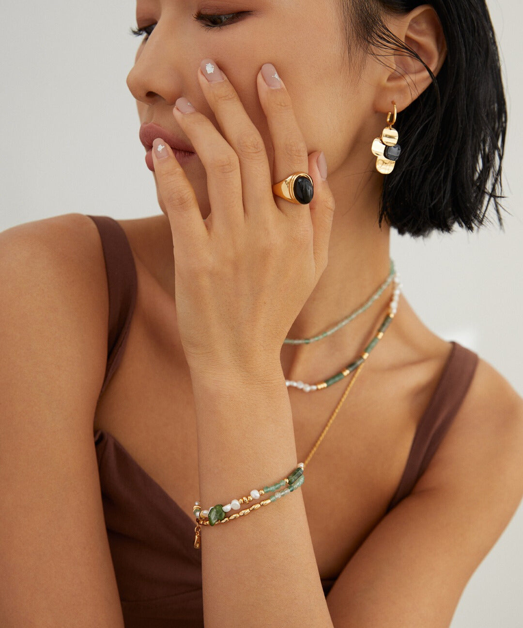 A model wearing a green and gold bracelet and necklace, complemented by a ring. Stunning jewelry ensemble.