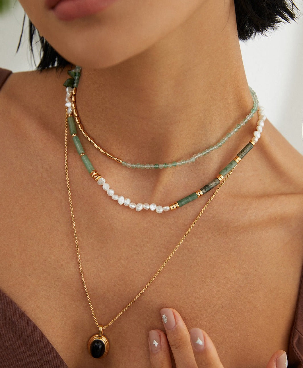 Woman wearing layered green and gold bead necklaces.