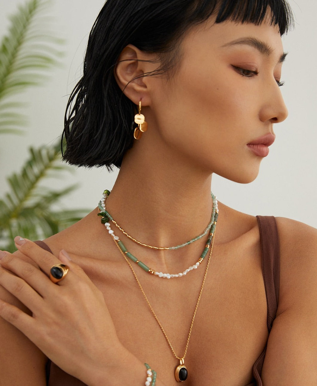 A woman adorns a layered necklace with a gold chain and a captivating black agate stone pendant.