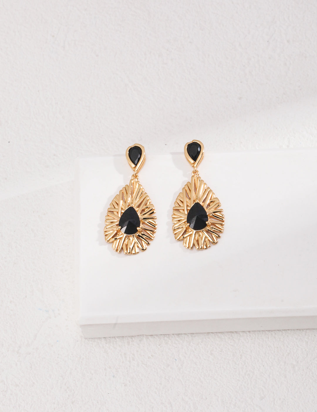 Elegant gold and black earrings on a white surface, exuding magic and mystery.