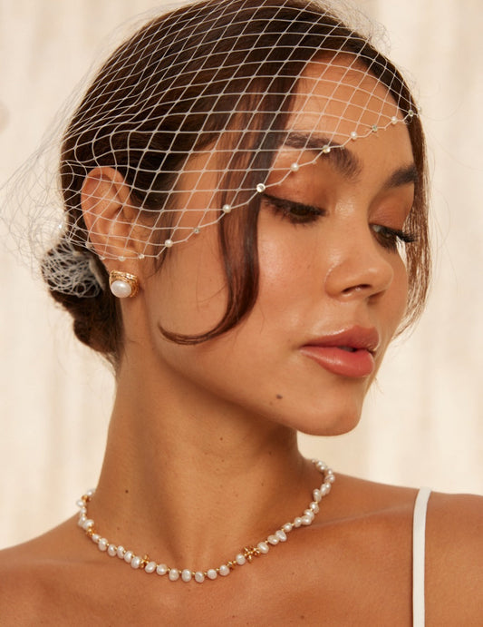 A woman wearing a veil and a pearl necklace, complemented by pearl stud earrings, showcasing a refined look.