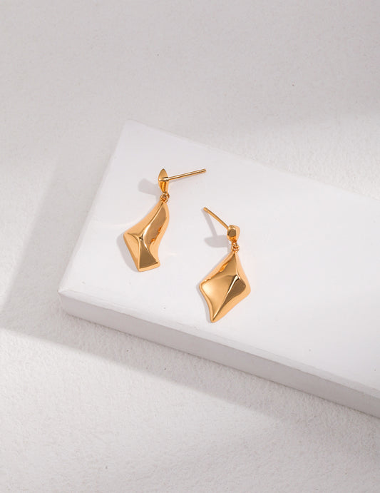 Stylish gold plated drop earrings placed on a white tabletop.