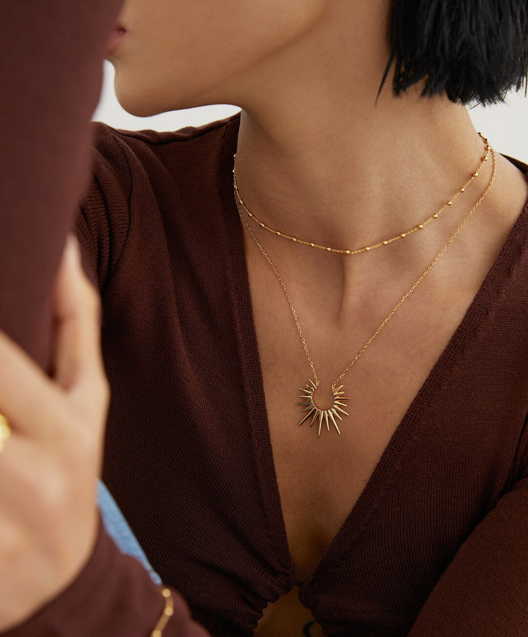 A model wearing a gold necklace, featuring a sunray pendant.