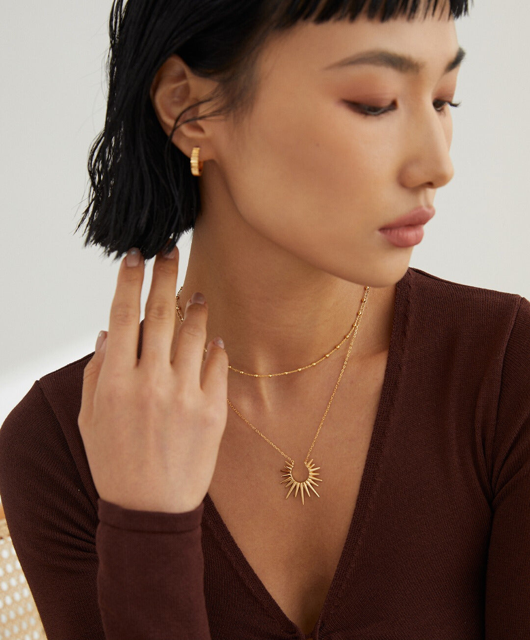 A woman wearing a gold sunray necklace and earrings, completing her elegant jewelry set.