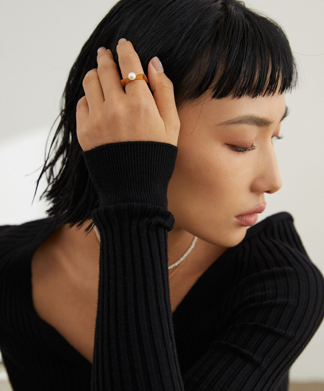 Stylish woman in black sweater flaunting a gold square ring with freshwater pearl.