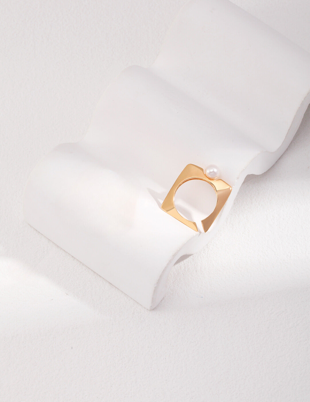 Gold square ring with freshwater pearl on white surface.