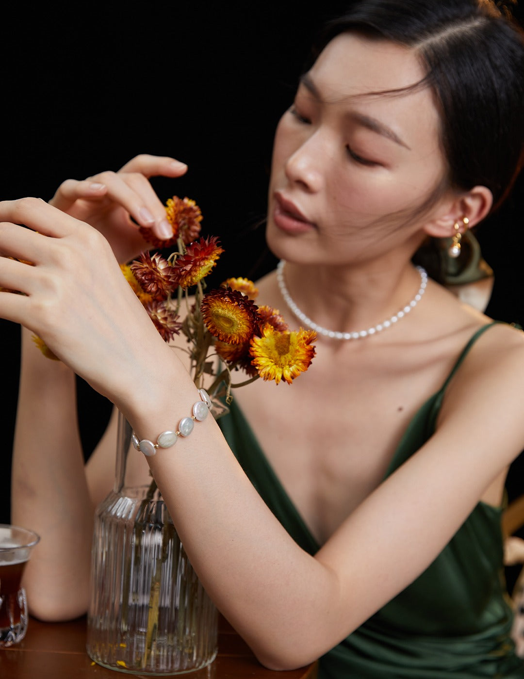 Lady in green dress with flowers, accessorized with pearl bracelet.