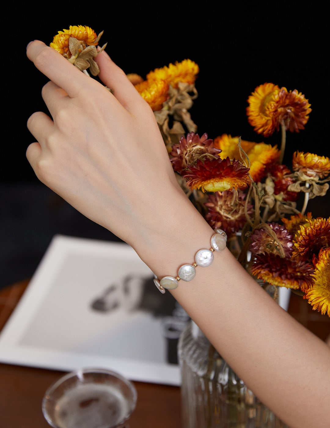 Hand wearing a bracelet with round baroque pearls, holding a flower