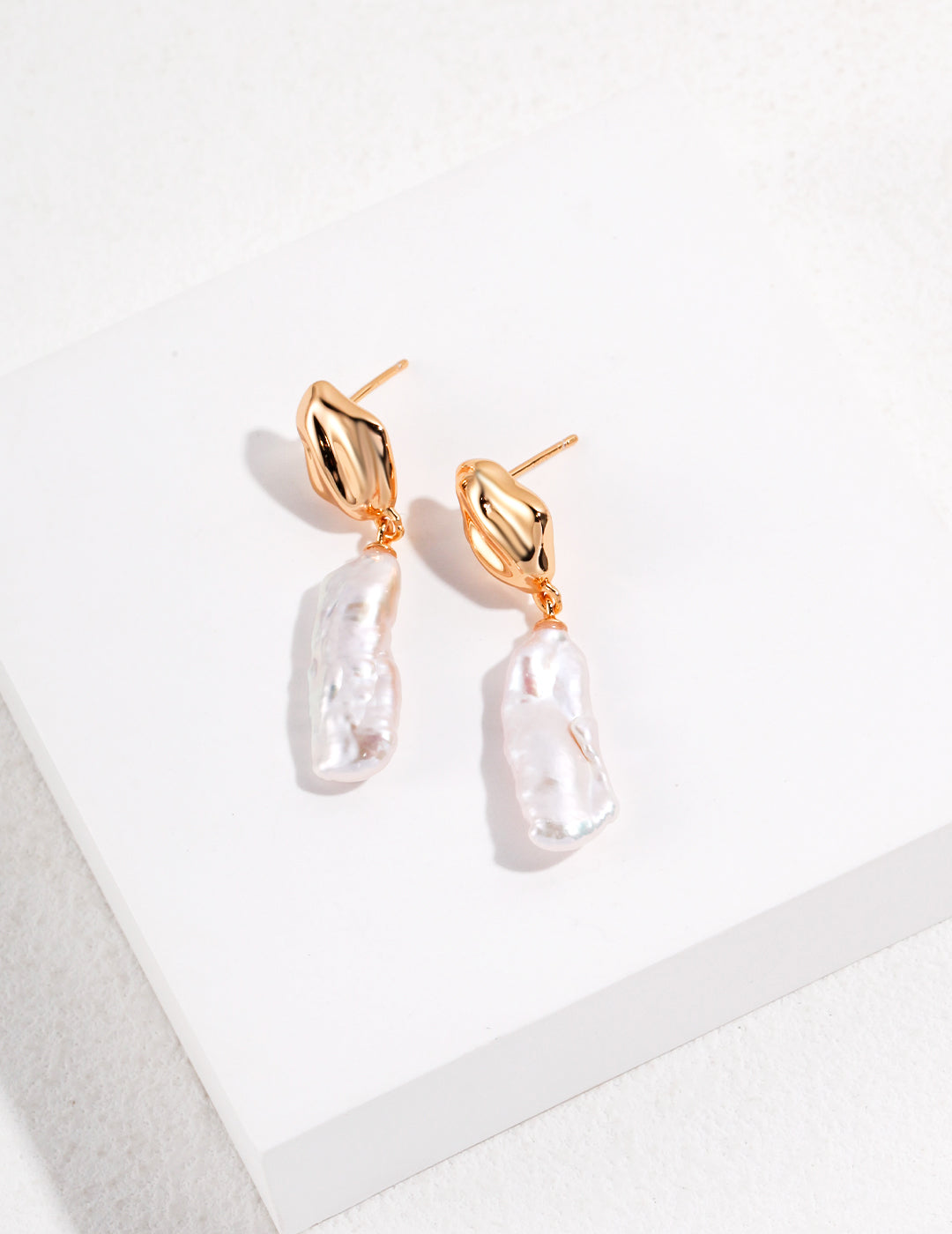 Elegant gold baroque pearl earrings beautifully positioned on a white surface.