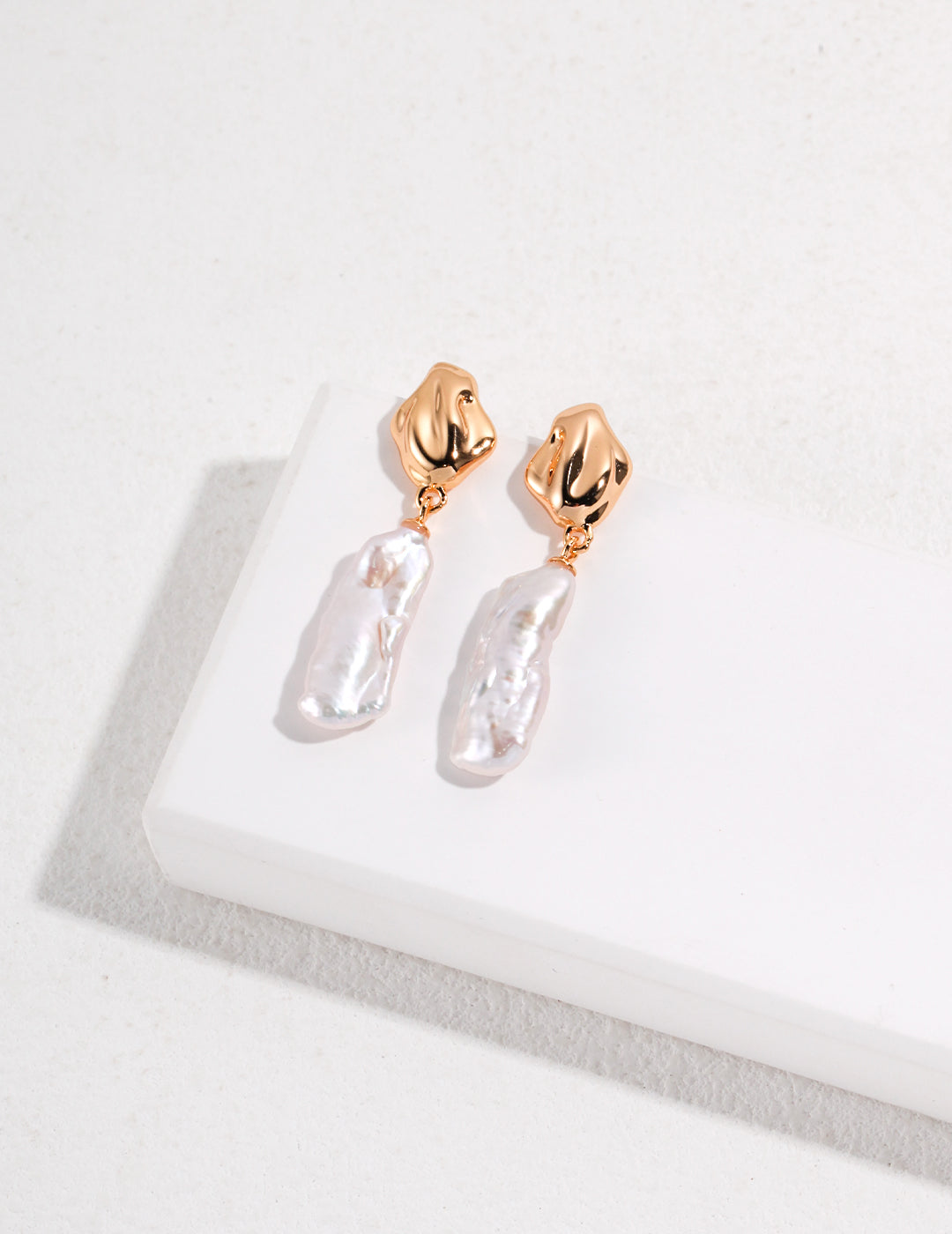 Gold baroque pearl earrings resting elegantly on a smooth white surface, showcasing their luxurious gold and white hues.