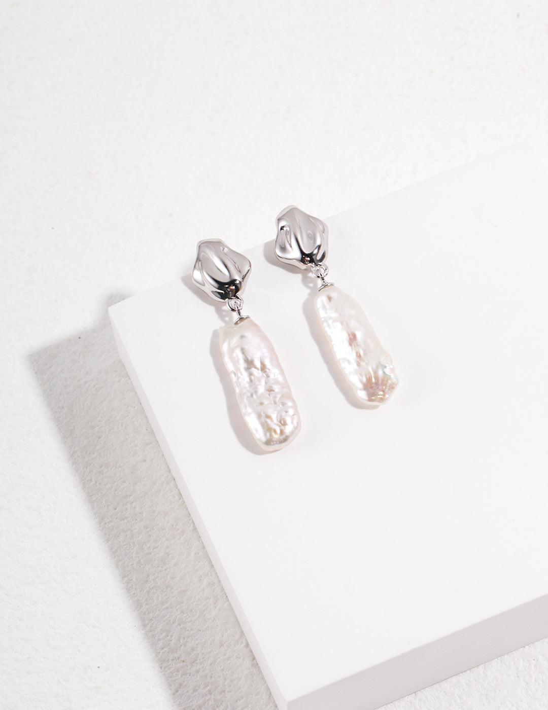 Beautiful silver baroque pearl earrings on a white surface, emphasizing their classic elegance and timeless appeal.