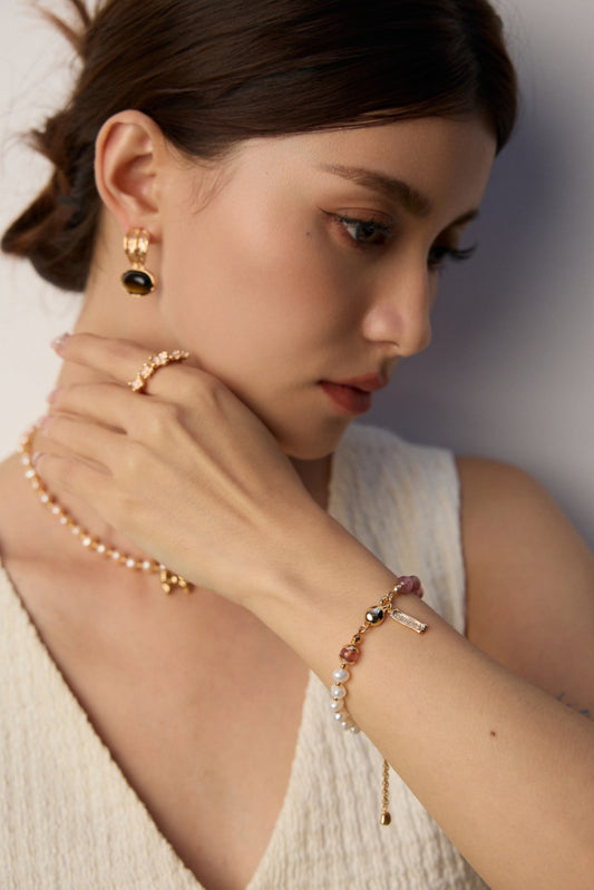 A woman in a white dress accessorized with a pearl necklace and a bracelet of pearls and strawberry quartz.
