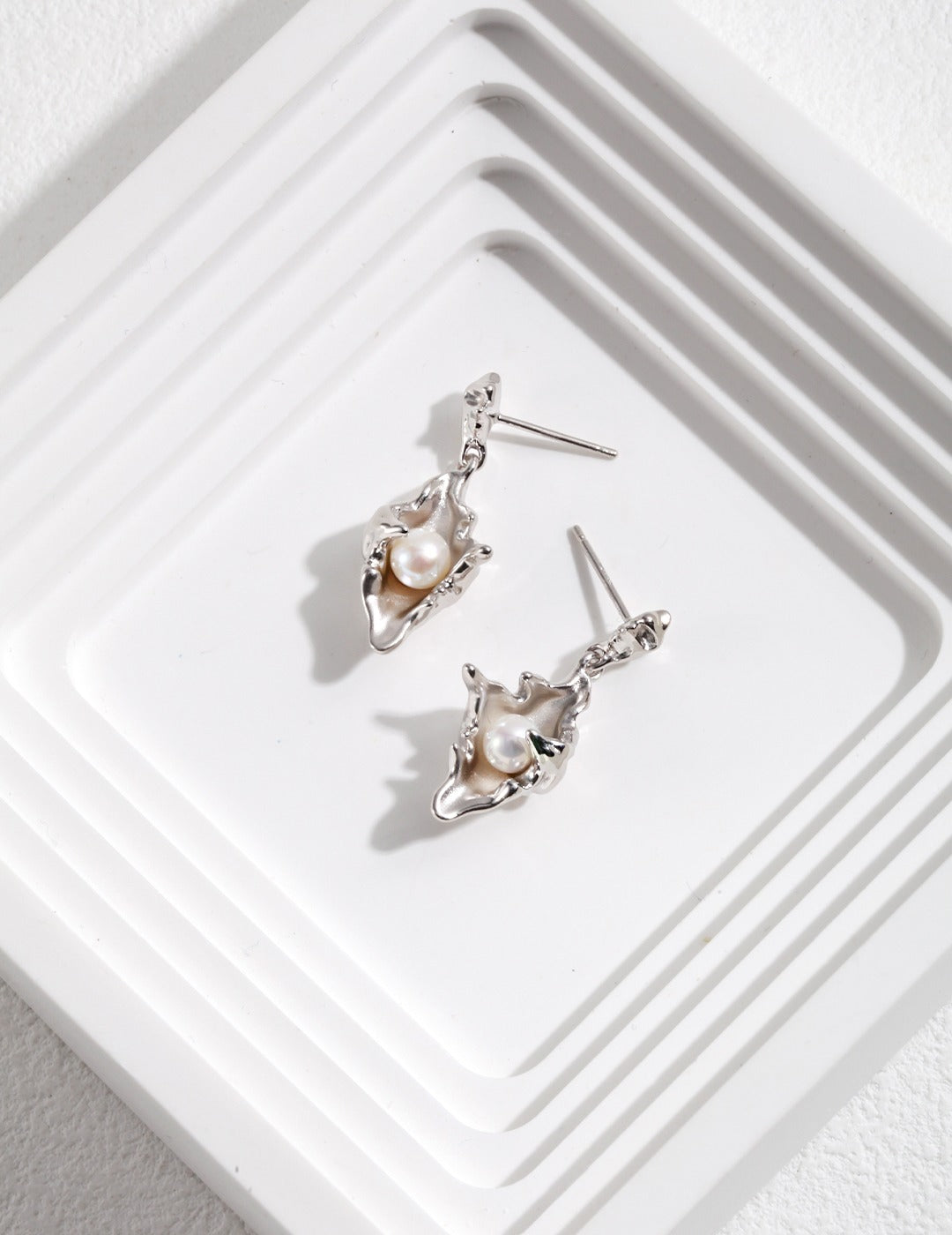 Silver plated conch earrings with freshwater pearls on a white tray.