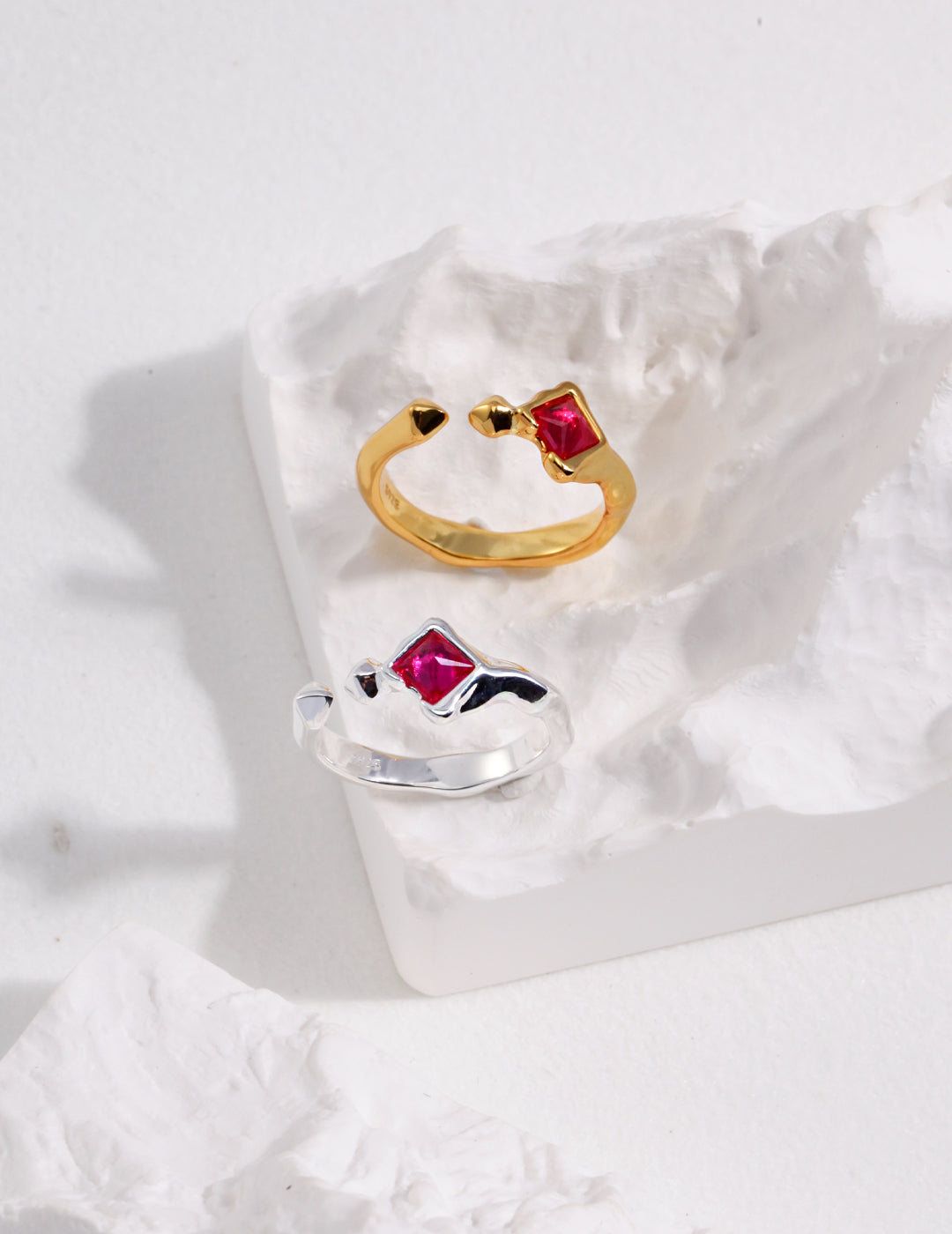 Silver and gold rings with lab-created rubies, displayed on a rock.