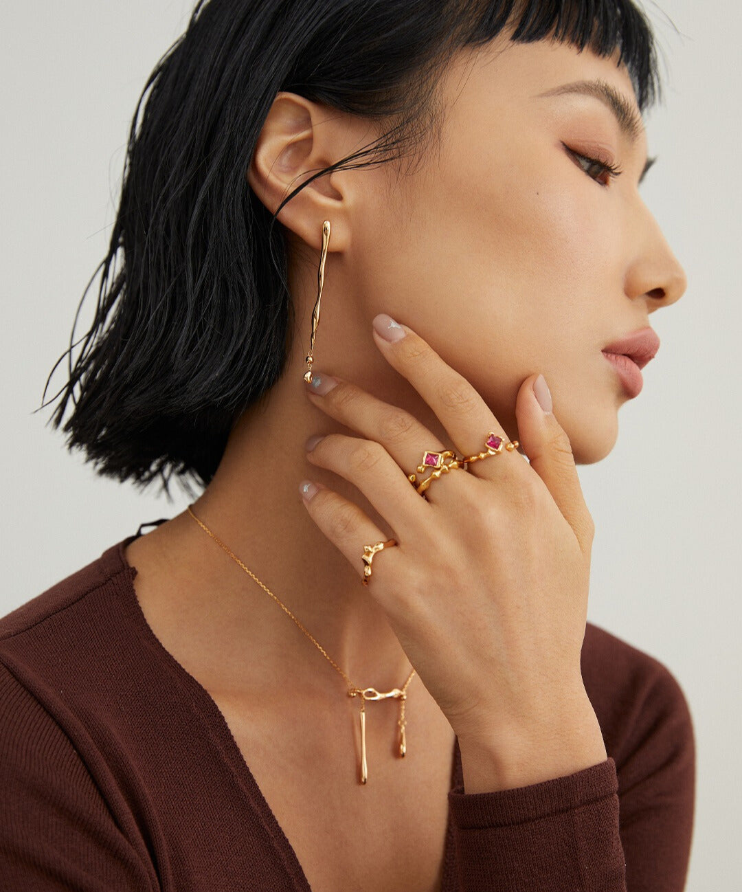 Woman wearing gold ring and earrings, with lab-created rubies and stacking rings.