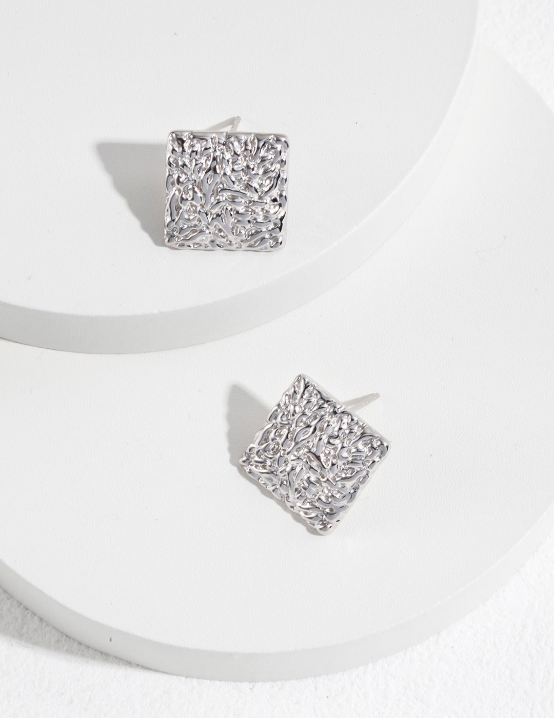 Silver square studs displayed on white surface.