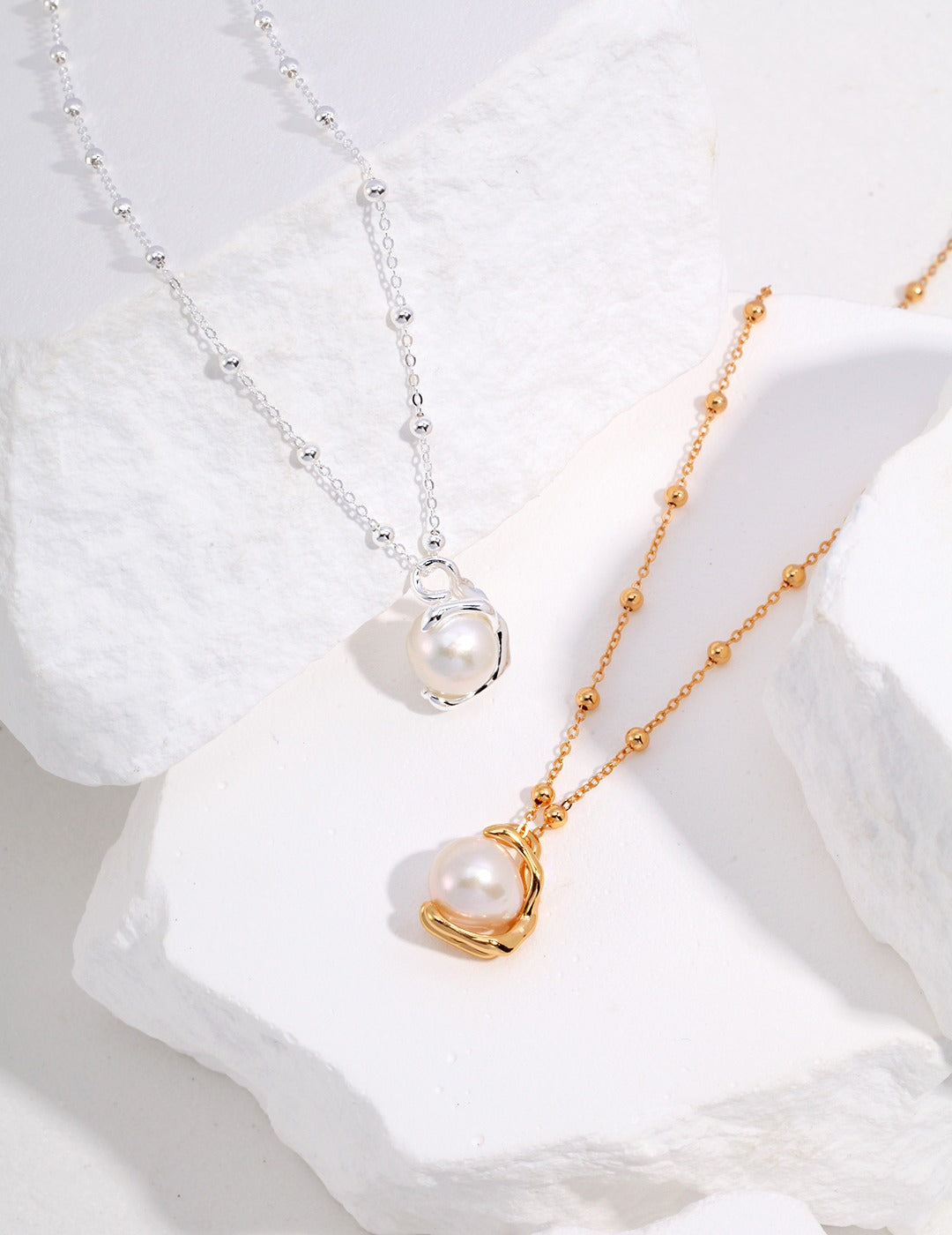 Two luxurious baroque pearl necklaces, one in silver and one in gold, showcased on a white surface.