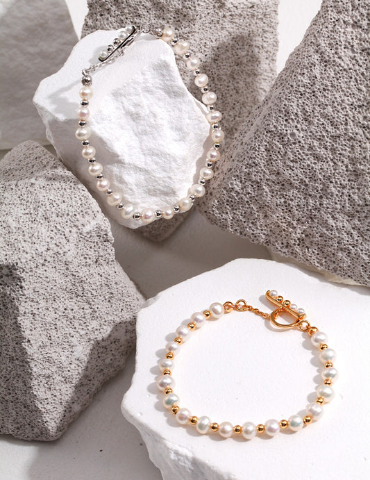 Pair of elegant bracelets with silver and gold freshwater pearls on rocks.