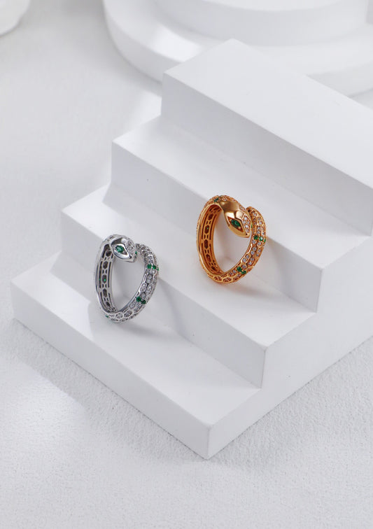 A close-up of two rings with green and gold stones on a white table; includes a silver and gold snake ring.