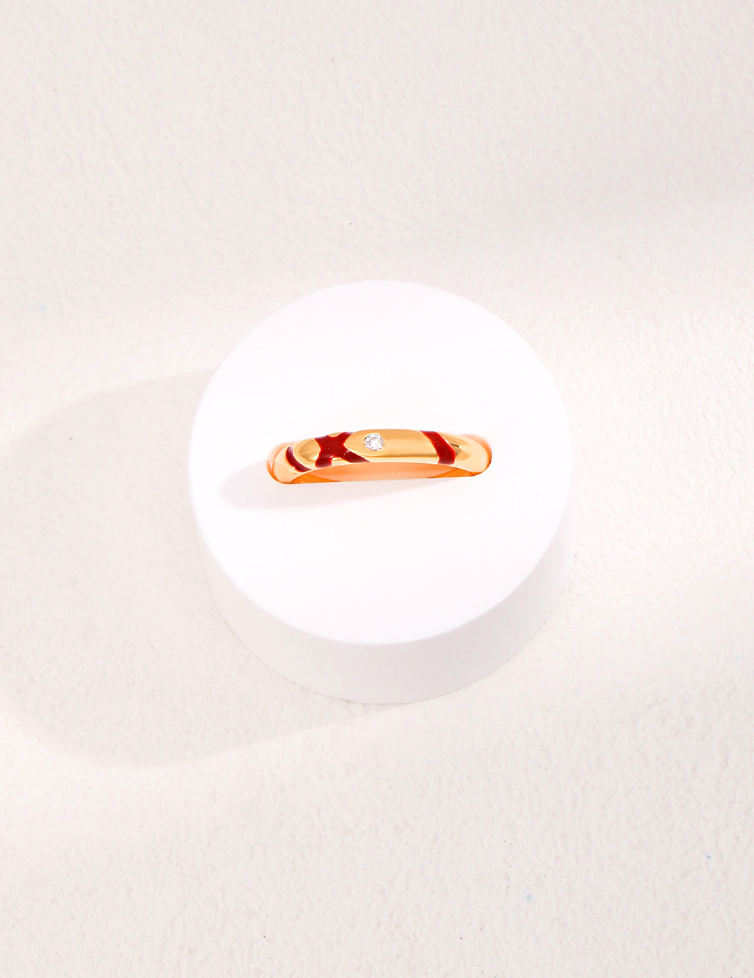 An exquisite gold plated ring featuring red accents and shimmering cubic zirconia, delicately positioned on a clean white plate.