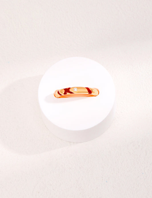 An exquisite gold plated ring featuring red accents and shimmering cubic zirconia, delicately positioned on a clean white plate.