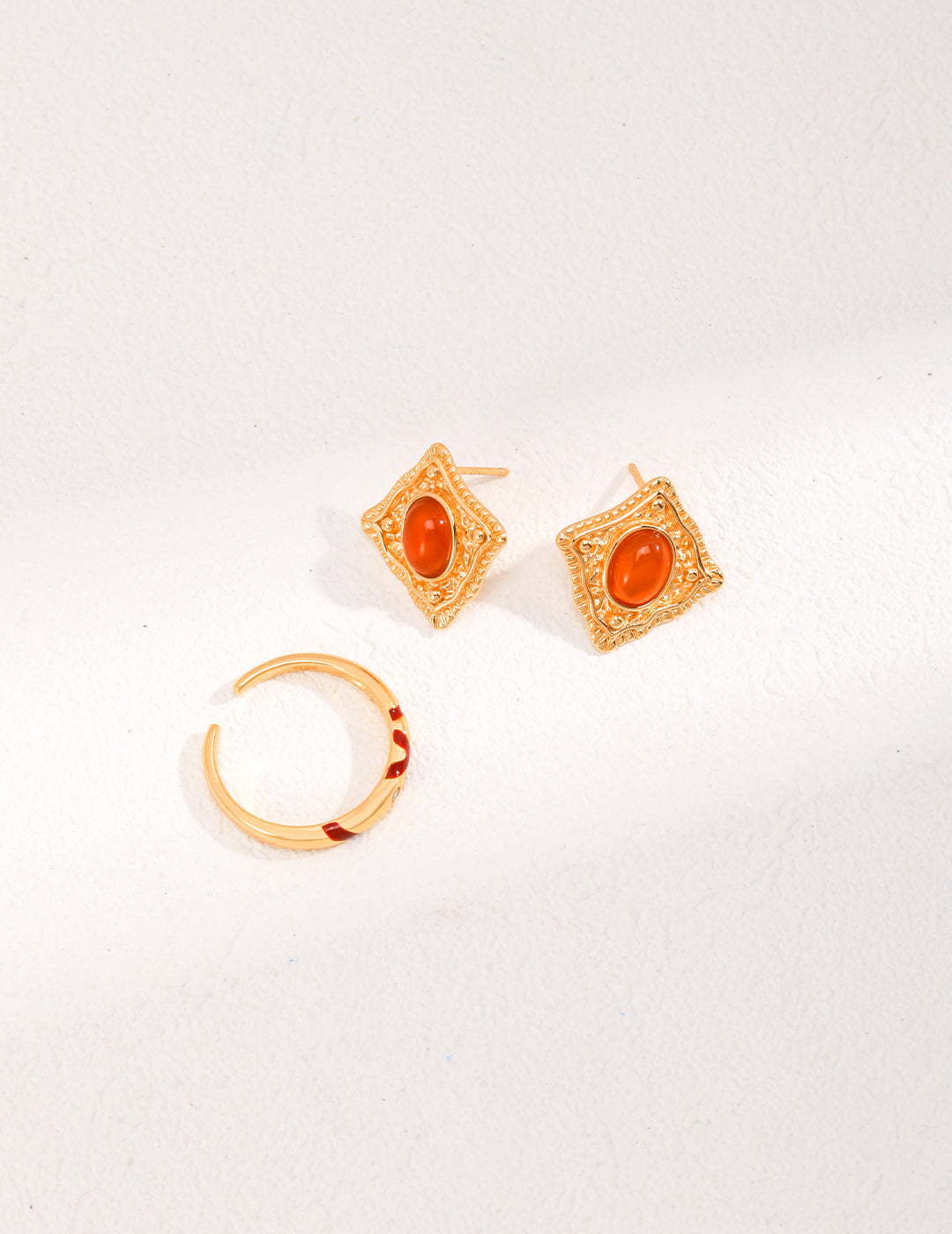 Two gold earrings and a ring with red stones: gold plated ring with red splashes and cubic zirconia, red agate earrings.