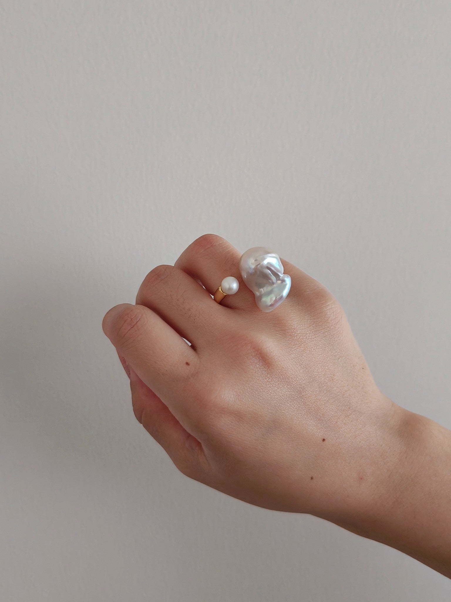 A person elegantly displays a baroque pearl ring on their hand, showcasing its unique shape and luster.