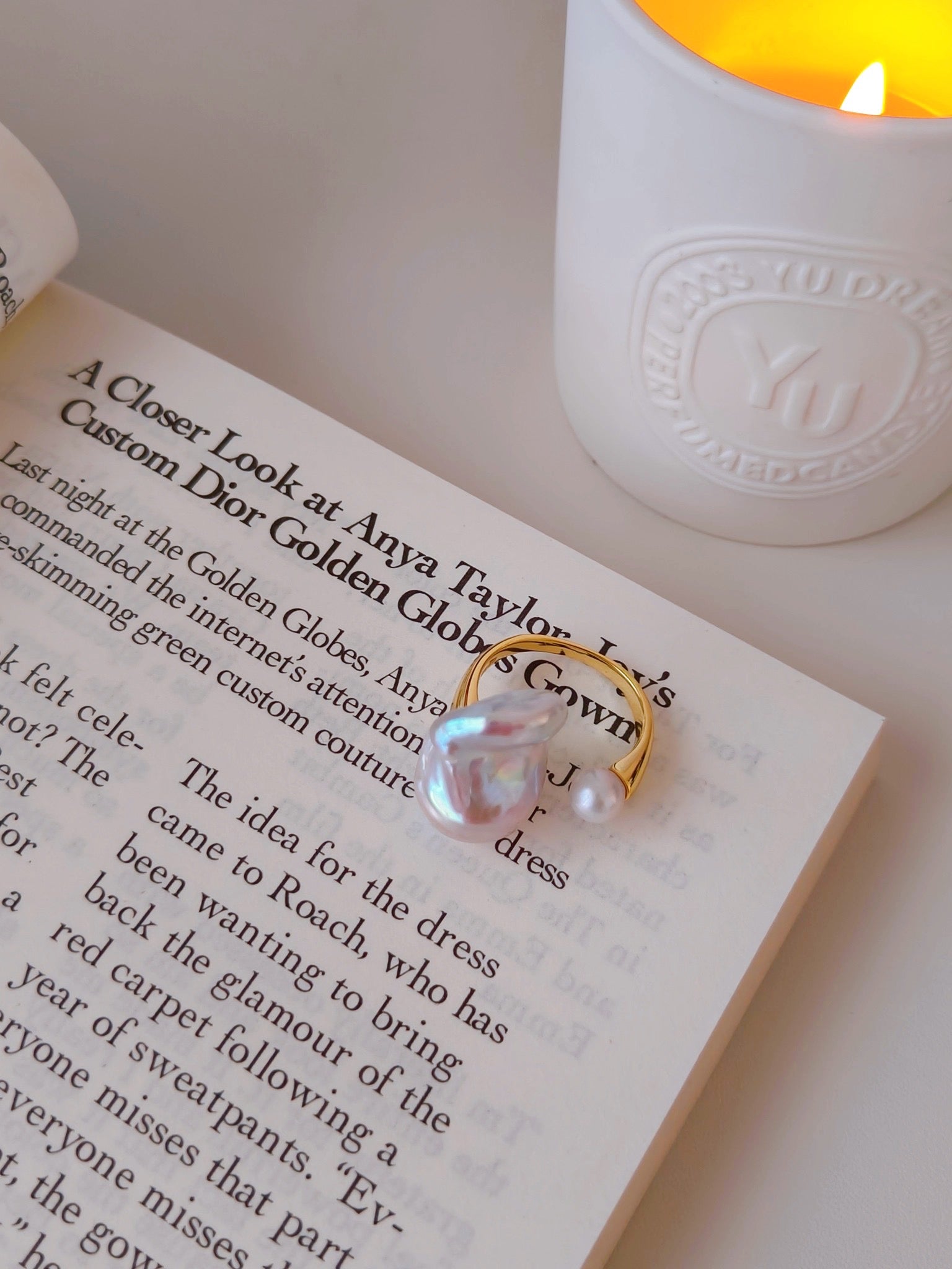 A book adorned with a baroque pearl ring and a flickering candle beside it, creating a warm, inviting atmosphere.