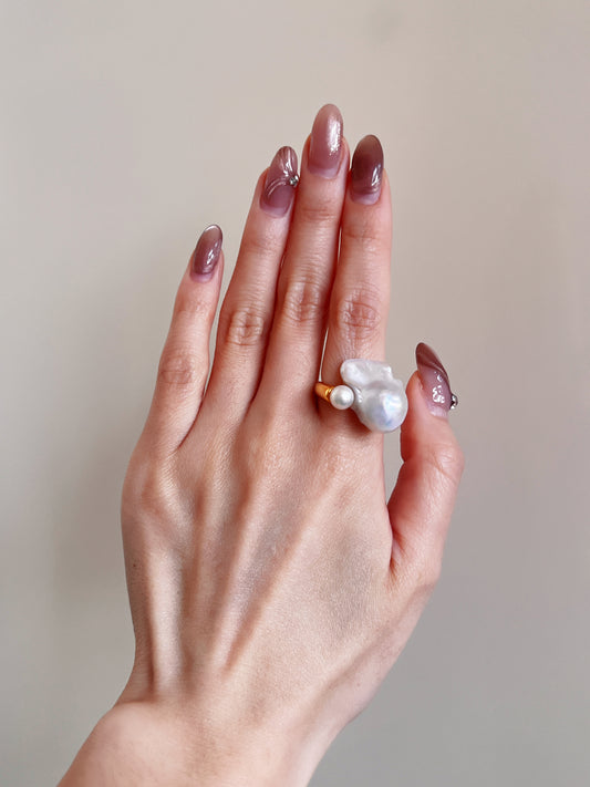 A person elegantly displays a baroque pearl ring on their hand, showcasing its unique shape and luster.