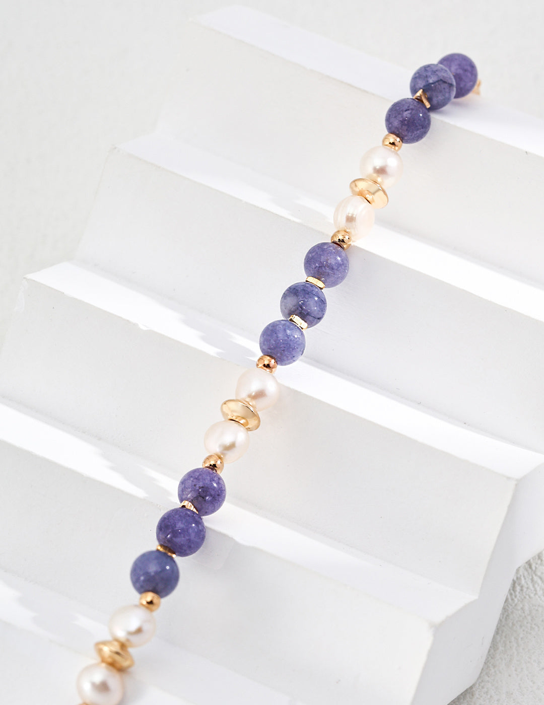 A chic kunzite bracelet in purple and white, embellished with gold beads, perfect for adding a touch of sophistication.