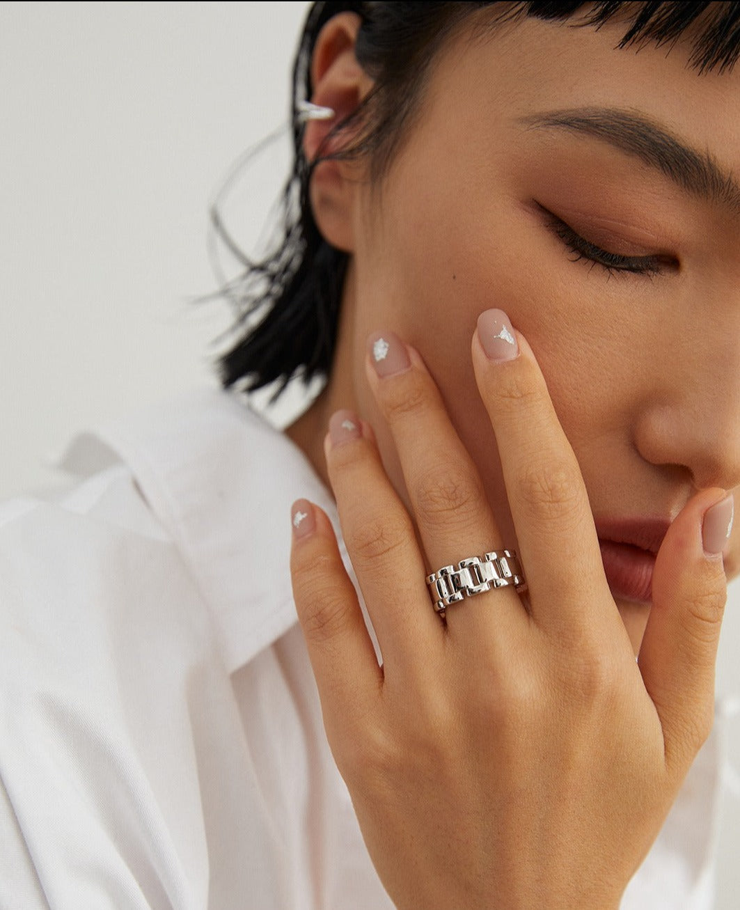 A woman wearing a white shirt with a silver ring on her hand.