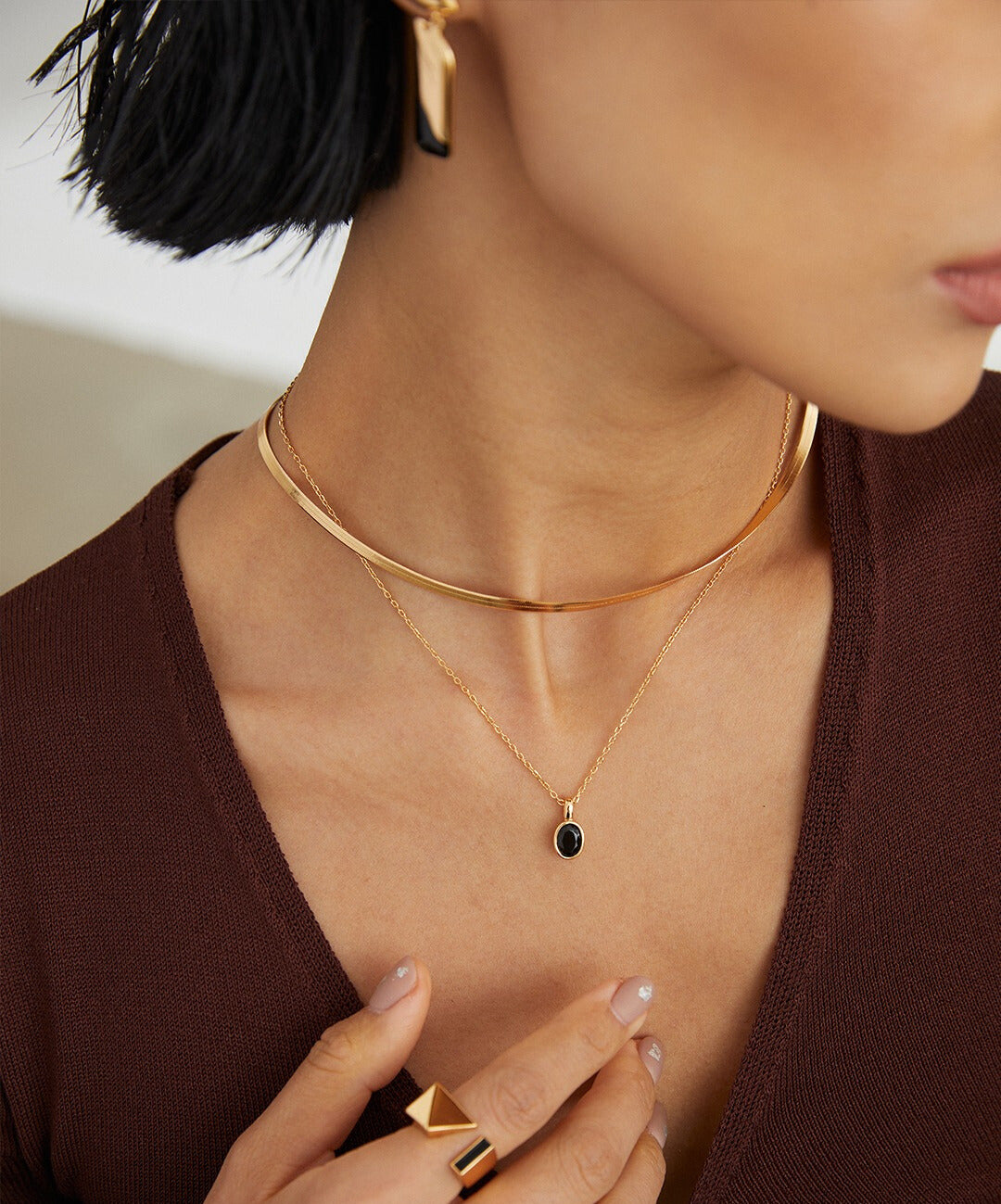 A woman wearing a gold necklace with a black agate necklace and a gold enamel ring.