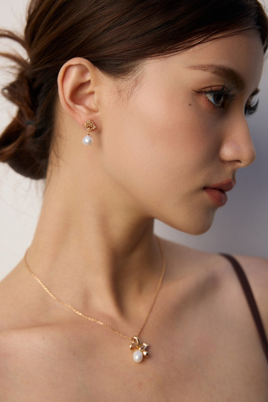 A woman adorned with a pearl and gold star necklace and elegant sculptural gold pearl earrings.