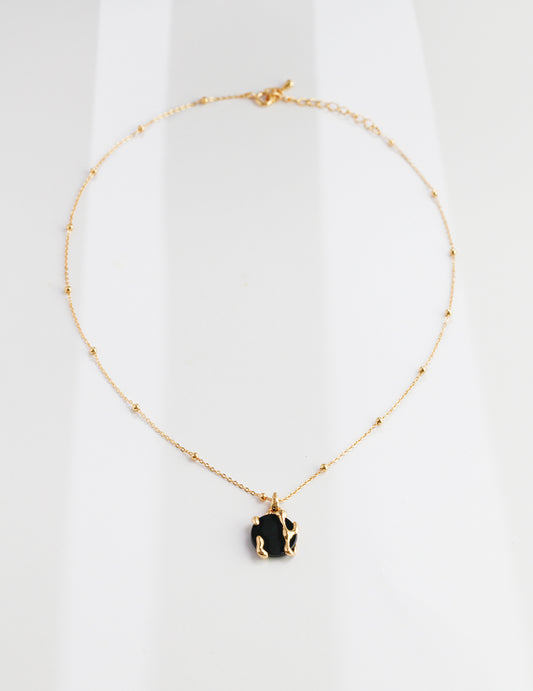 A gold chain holds a black stone necklace with a black agate pendant, creating an elegant and stylish accessory.