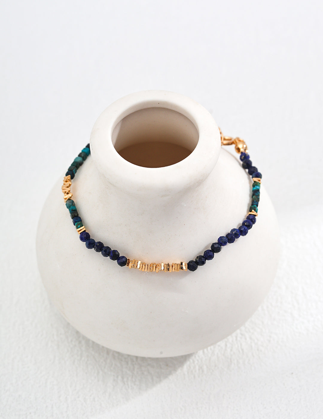 A white vase adorned with a blue and gold bracelet, creating a striking visual of color and design harmony.