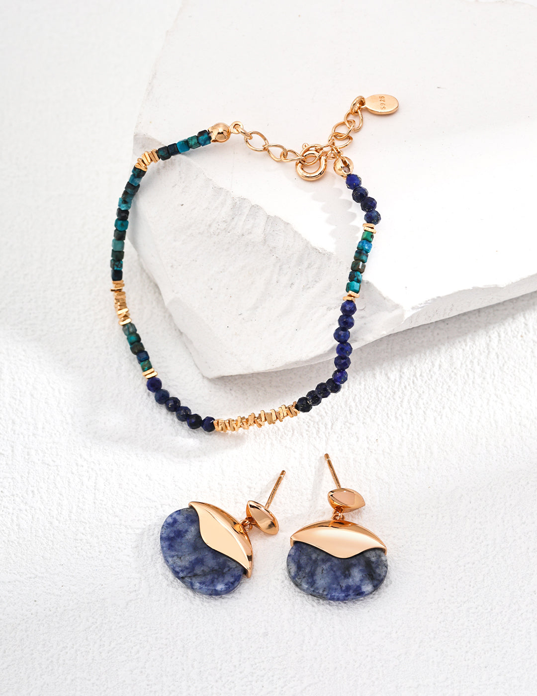 A stylish blue stone bracelet alongside earrings, both resting on a pristine white background.