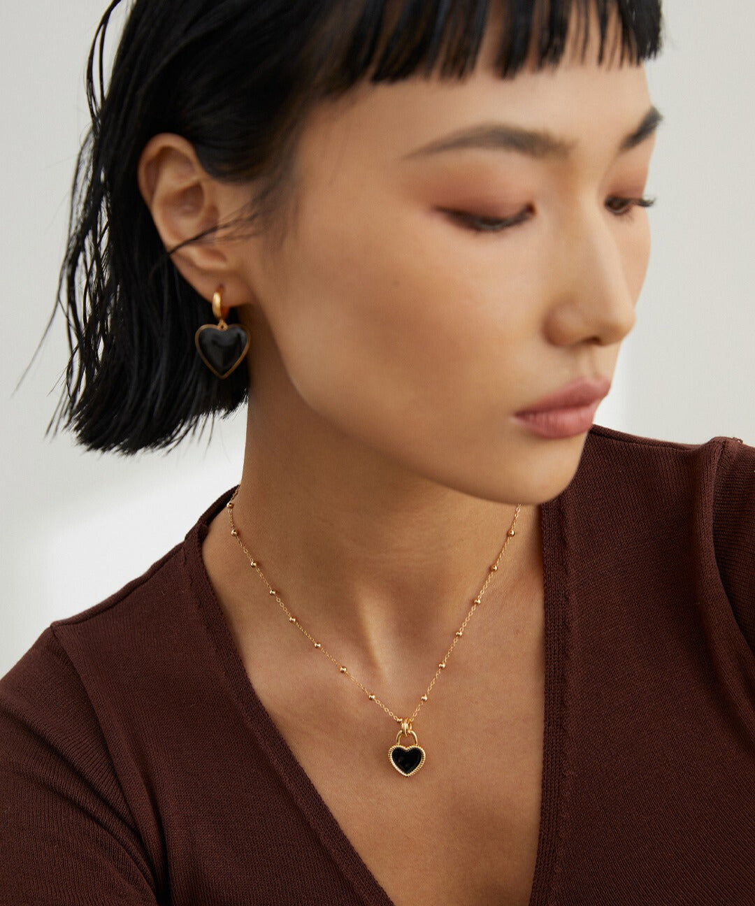 Model accessorized with black necklace and earrings, featuring gold plated heart pendant.