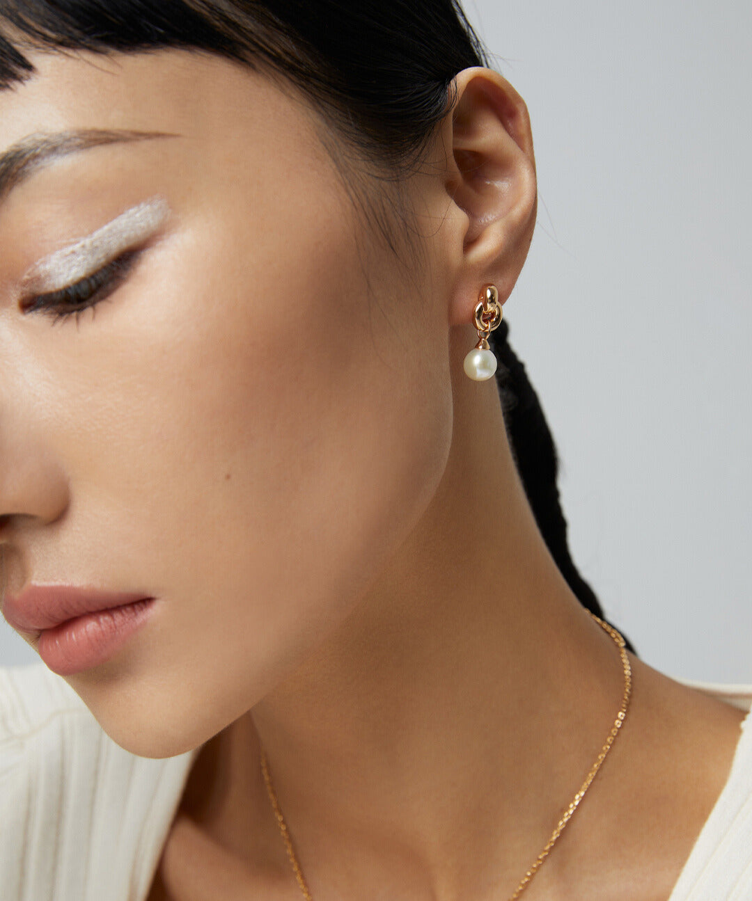 Gold jewelry set on woman, including necklace and earrings with interlocked knot and pearl.